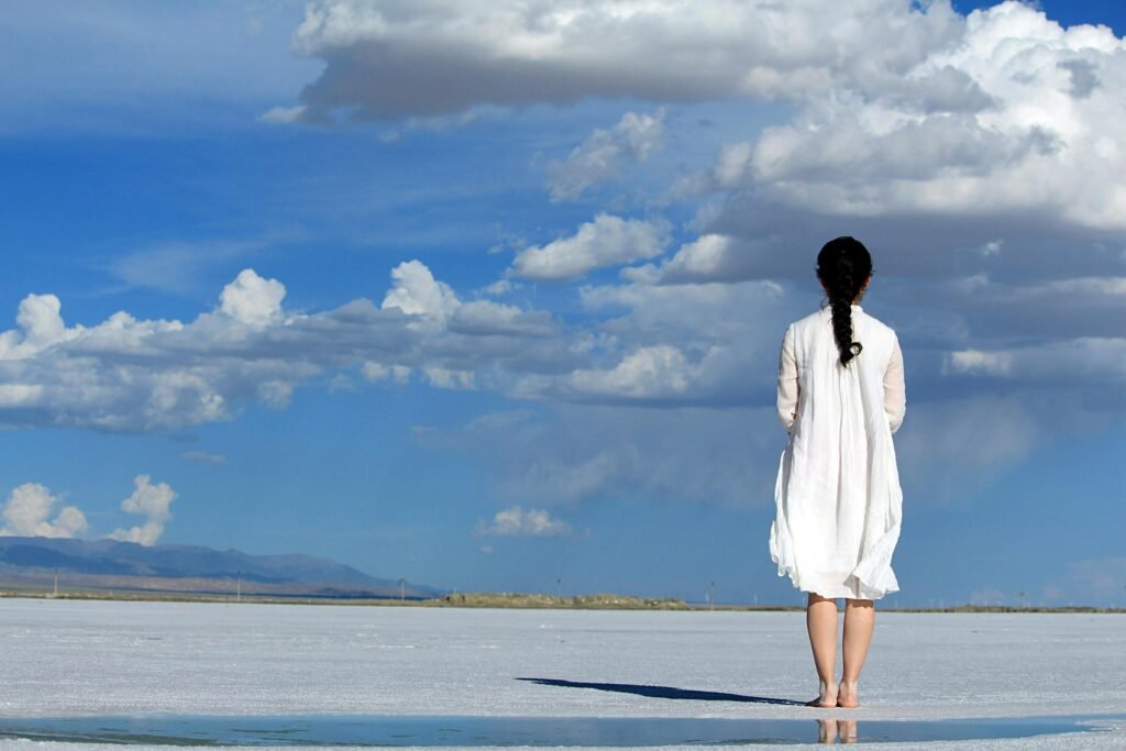 Woman stands alone on a vast salt flat under a bright blue sky with clouds.